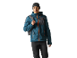 Homem com casaco azul com fechos laranja, gorro preto e mochila.