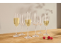 Sete flutes de champanhe, três cheias de vinho espumante, e três framboesas numa mesa de madeira.