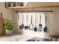 Utensílios de cozinha pendurados num varão acima de uma bancada com plantas e prateleira.