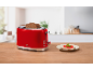 Torradeira vermelha com torradas e uma sanduíche de tomate e manjericão numa mesa de madeira.