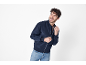 Homem sorridente com casaco bomber azul escuro e jeans.