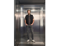 Homem com colete acolchoado preto, t-shirt cinzenta e jeans num elevador