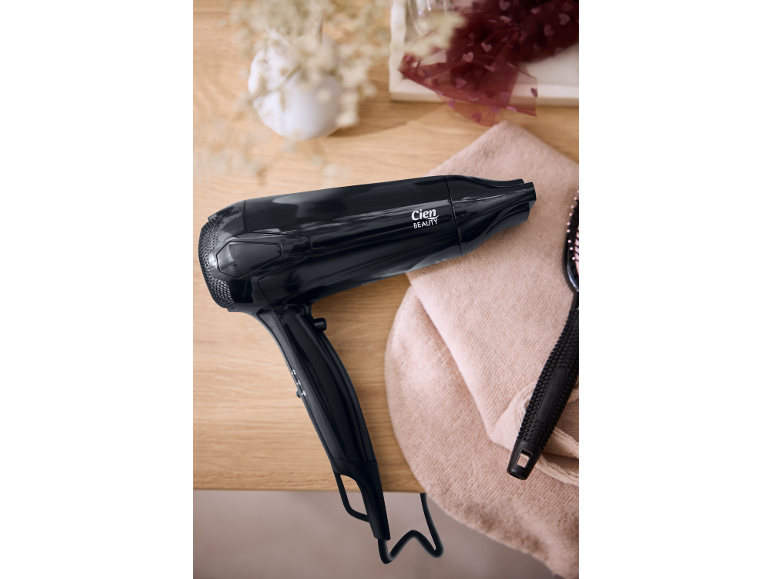 Secador de cabelo preto e escova numa mesa de madeira com uma toalha rosa.