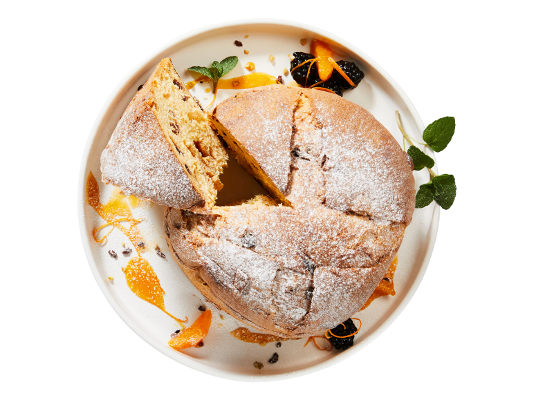 Panettone com açúcar em pó, pedaços de fruta cristalizada e decoração de hortelã e laranja.