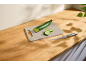 Pepino e fatias numa tábua de corte bege com faca numa bancada de madeira.