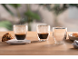 Três copos de espresso de parede dupla, dois com café fumegante, um vazio, com biscotti.