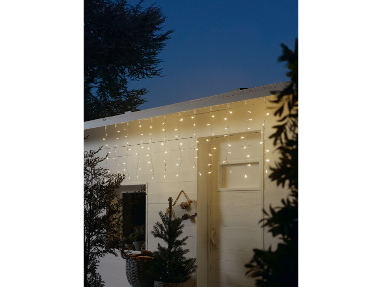 Luzes de corda tipo cascata numa cabana de madeira branca, decorada para o Natal