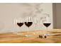 Copos de vinho tinto, alguns cheios de vinho, numa mesa de madeira com uvas.