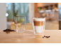 Copo de latte com grãos de café e um copo vazio sobre uma mesa de madeira.