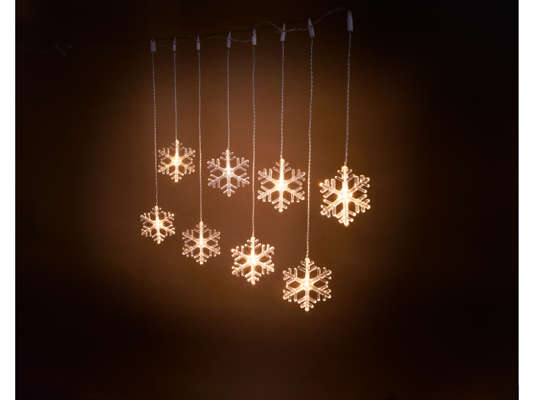 Luzes de corda de flocos de neve iluminadas contra um fundo escuro.