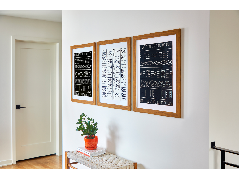 Três quadros emoldurados de madeira com padrões a preto e branco, um banco com uma planta.