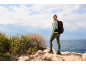 Mulher com roupa de caminhada e mochila num penhasco rochoso com vista para o mar.