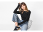 Mulher de top preto de manga comprida, jeans largos e sapatilhas sentada numa cadeira.