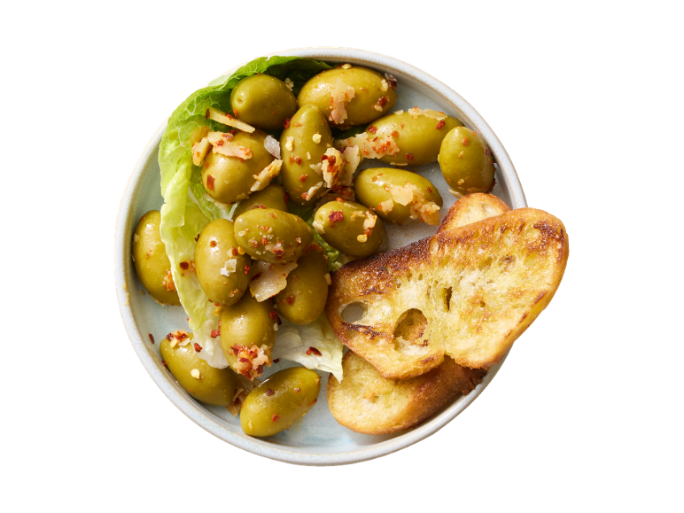 Azeitonas verdes marinadas com chili e alho, servidas com fatias de pão torrado.
