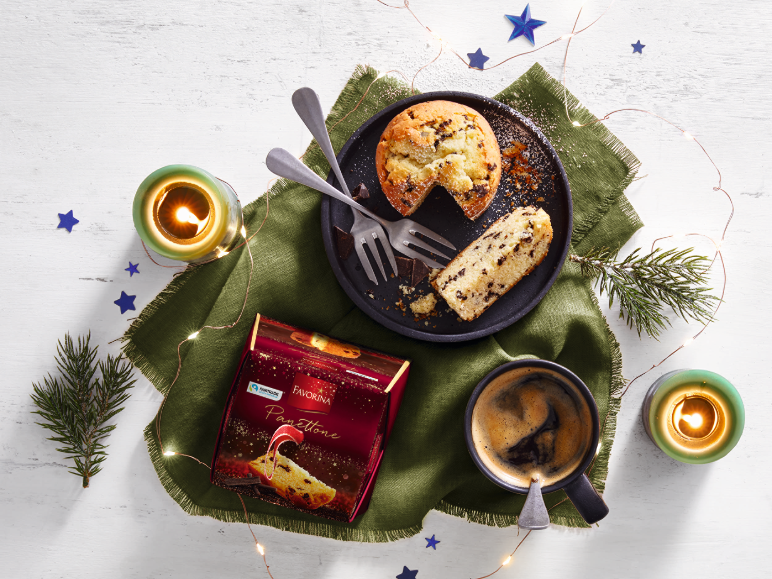 Panettone, café e decorações de Natal com velas numa mesa de madeira branca.