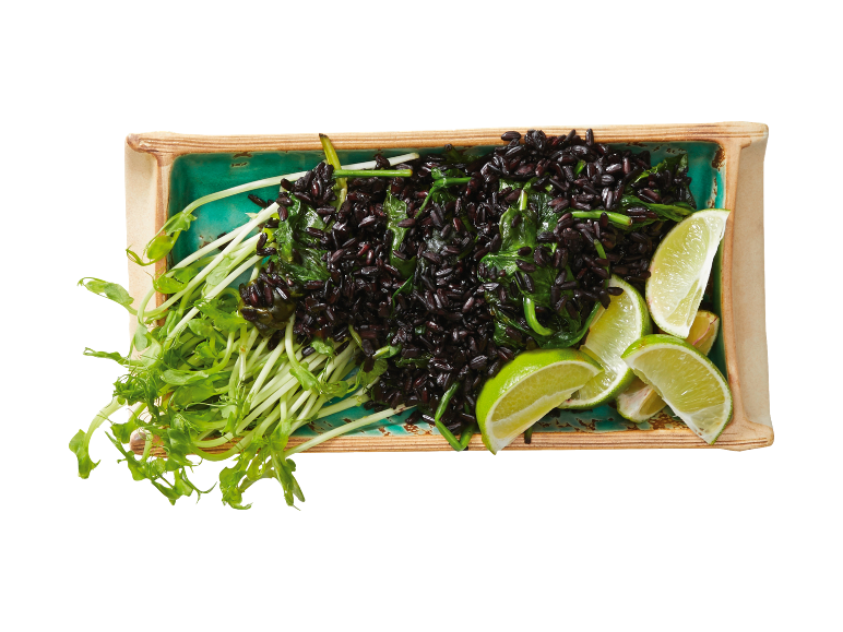 Arroz preto com espinafres, rebentos verdes e lima num prato retangular.