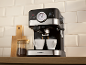 Máquina de café expresso preta e prateada a fazer café em duas chávenas brancas, com um frasco de café moído ao lado.