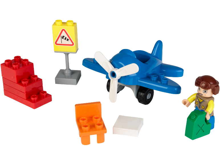 Avião de brinquedo, figura de piloto, blocos vermelhos, sinal de biruta, cadeira laranja e bloco branco.