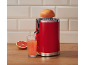 Espremedor de citrinos vermelho com uma toranja espremida e um copo de sumo numa bancada de madeira.