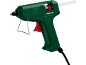 Pistola de cola quente verde com gatilho vermelho e suporte de metal, com um bastão de cola branco.