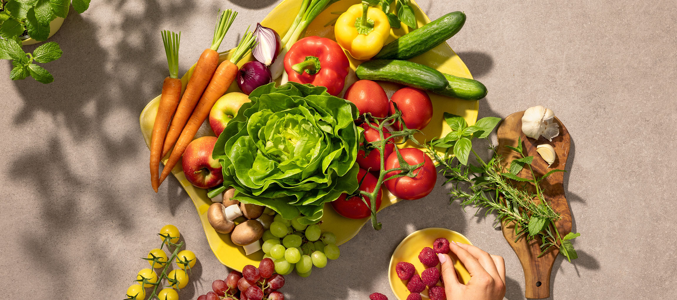 Vegetais e frutas frescas numa travessa amarela, incluindo alface, tomates, cenouras e bagas.