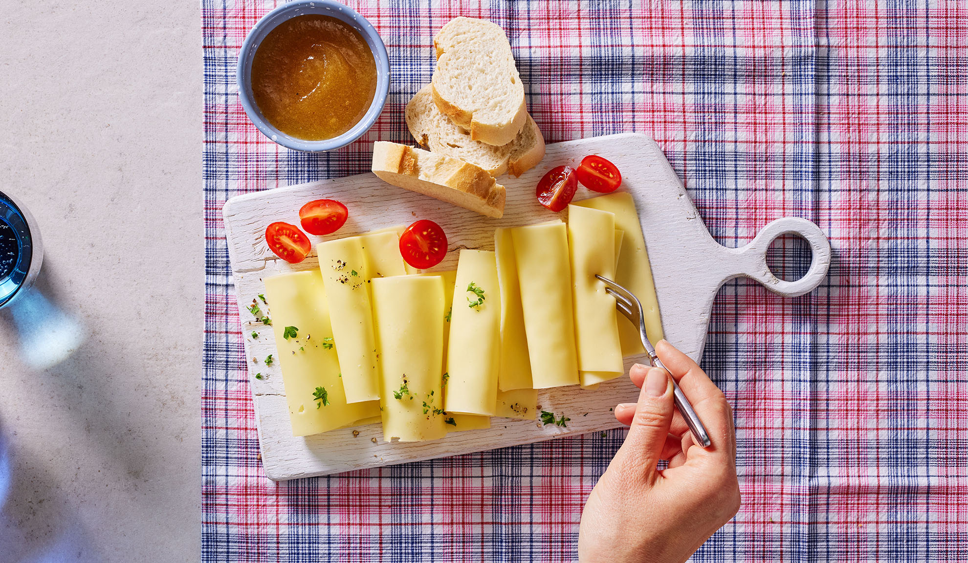 Fatias de queijo, tomate cereja, pão e compota numa tábua de servir.