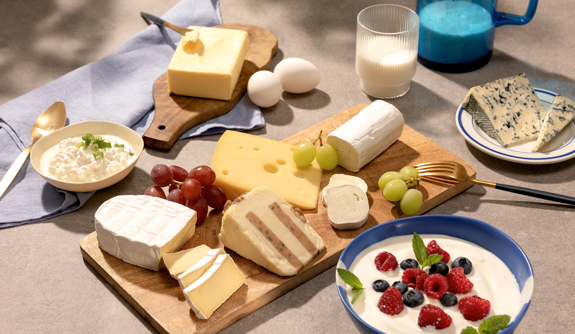 Uma variedade de queijos, uvas e laticínios como queijo cottage, leite e iogurte com frutas vermelhas.