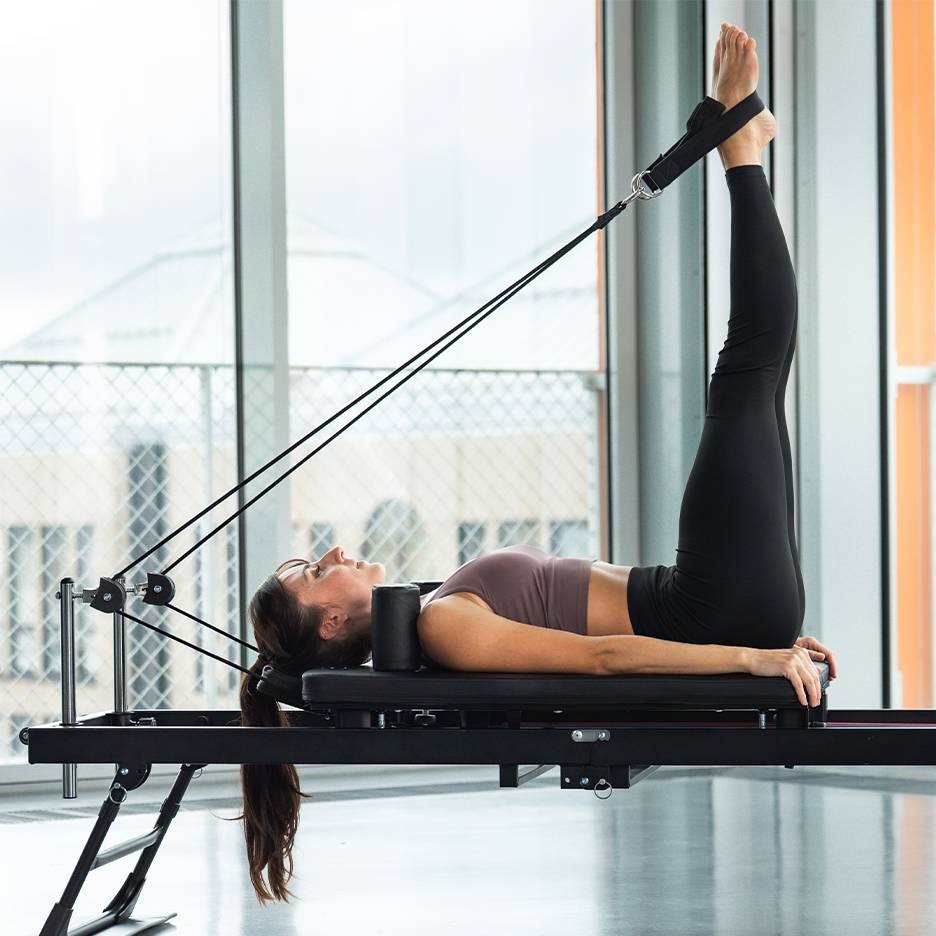 Mulher a fazer exercício de pernas numa máquina de Pilates reformer.