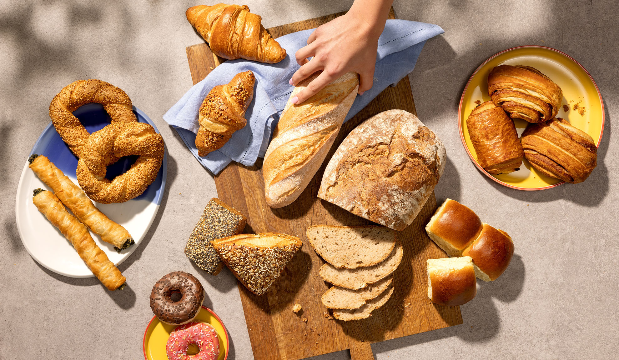 Variedade de produtos de panificação frescos, incluindo pão, croissants, doces e donuts numa mesa.