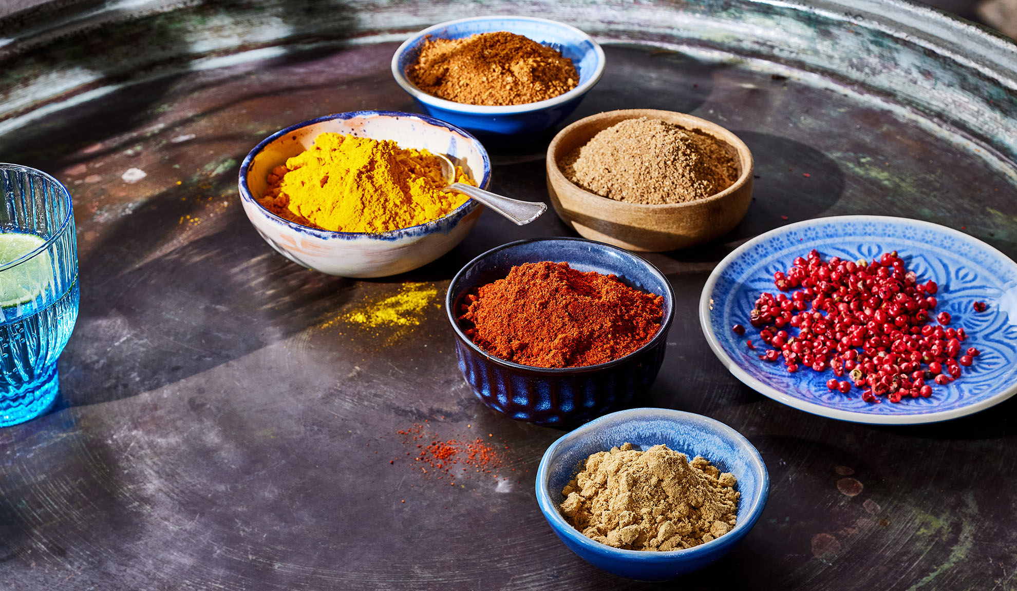 Várias especiarias em tigelas: açafrão, colorau, pimenta e outras numa bandeja de metal.
