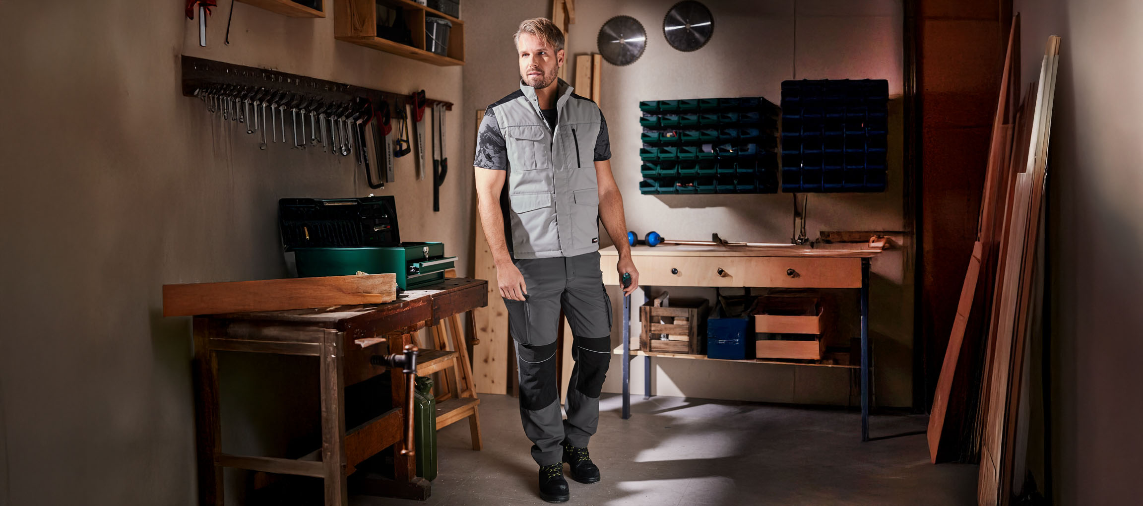 Um homem com roupa de trabalho e colete está numa oficina.