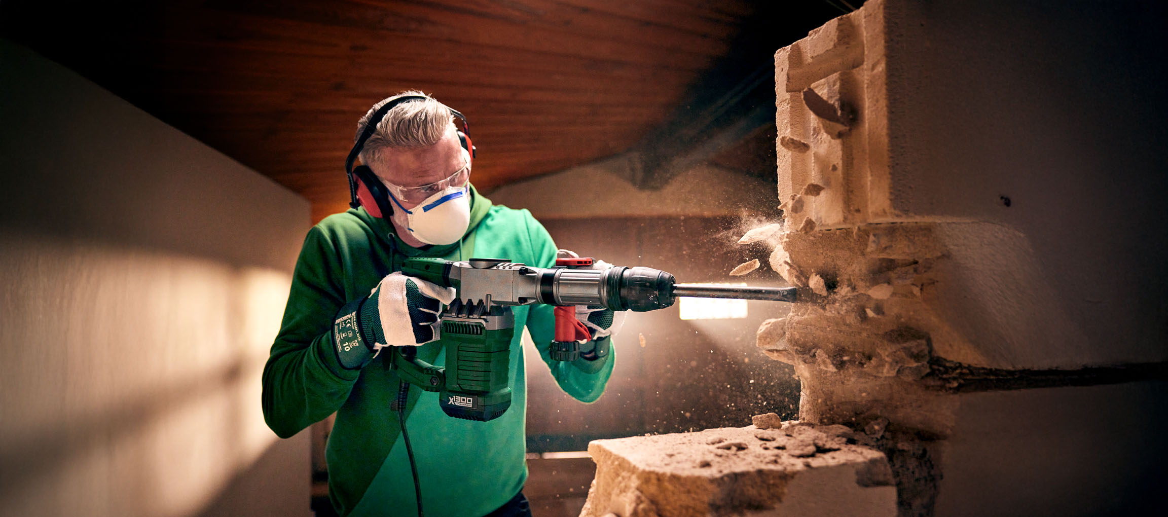 Um homem usa um martelo demolidor Bosch X1300 para demolir uma parede de blocos de concreto.