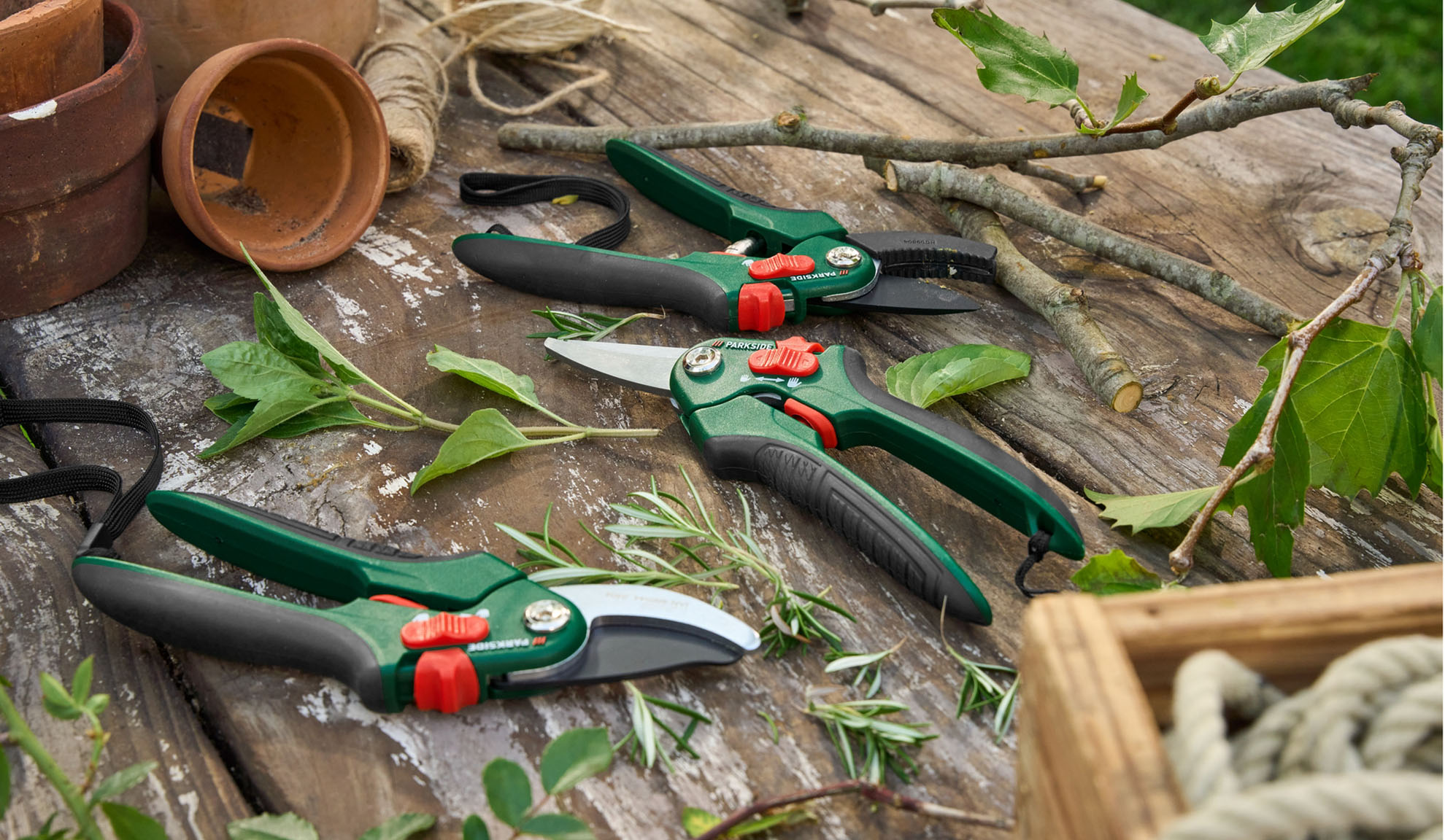 Tesouras de jardinagem e podões Parkside sobre uma superfície de madeira rústica com plantas e suprimentos de jardinagem.