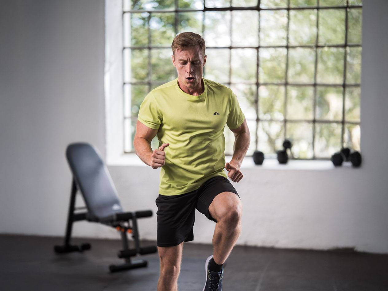 Homem de camiseta amarela e shorts pretos correndo em uma academia.