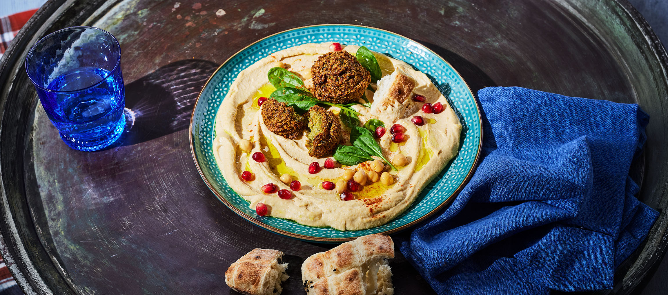 Hummus com falafel, sementes de romã e pão numa bandeja de metal.