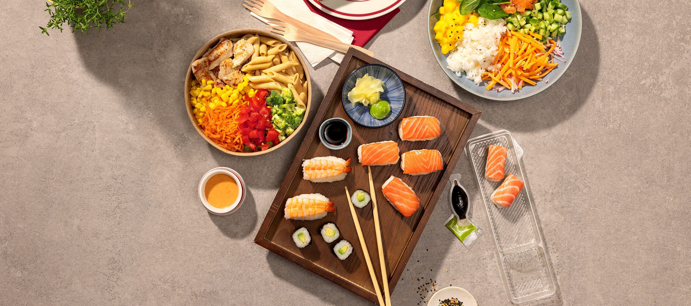 Pratos variados: tigela de massa e frango, sushi e uma poke bowl numa mesa.