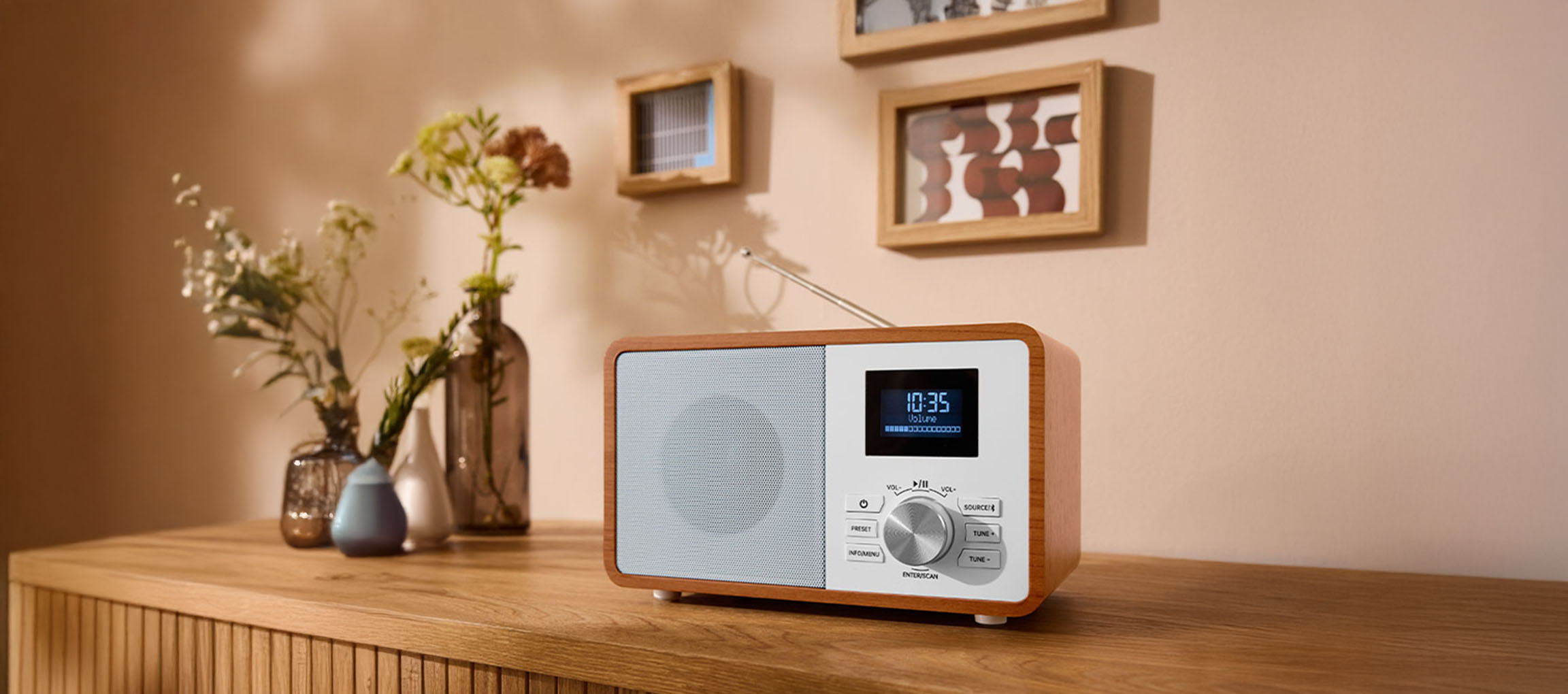 Um rádio digital de madeira em uma cômoda, com vasos e quadros na parede.