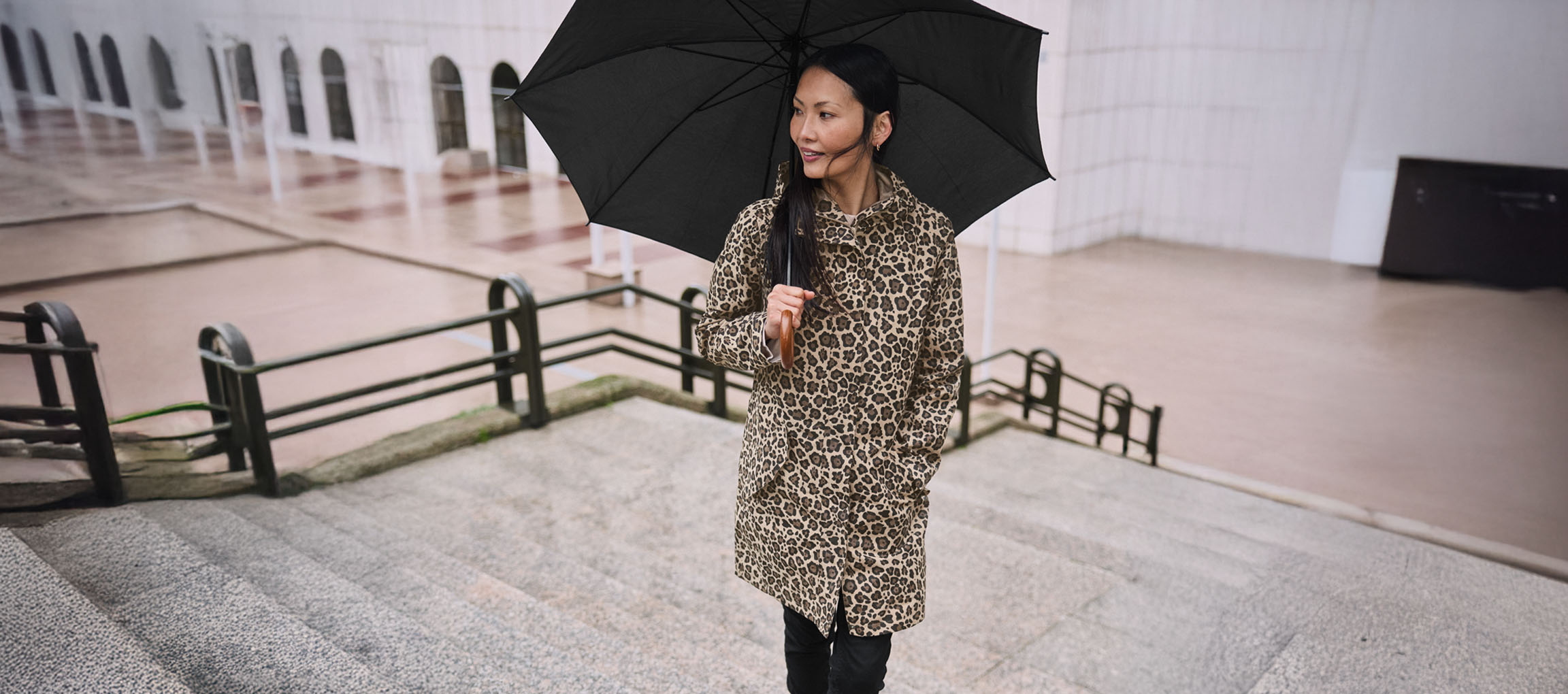 Mulher de casaco estampado de leopardo com guarda-chuva na escada.