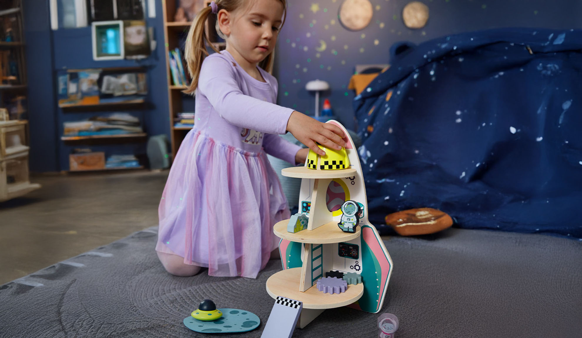 Uma menina brinca com um foguete de brinquedo e acessórios espaciais em um quarto temático.