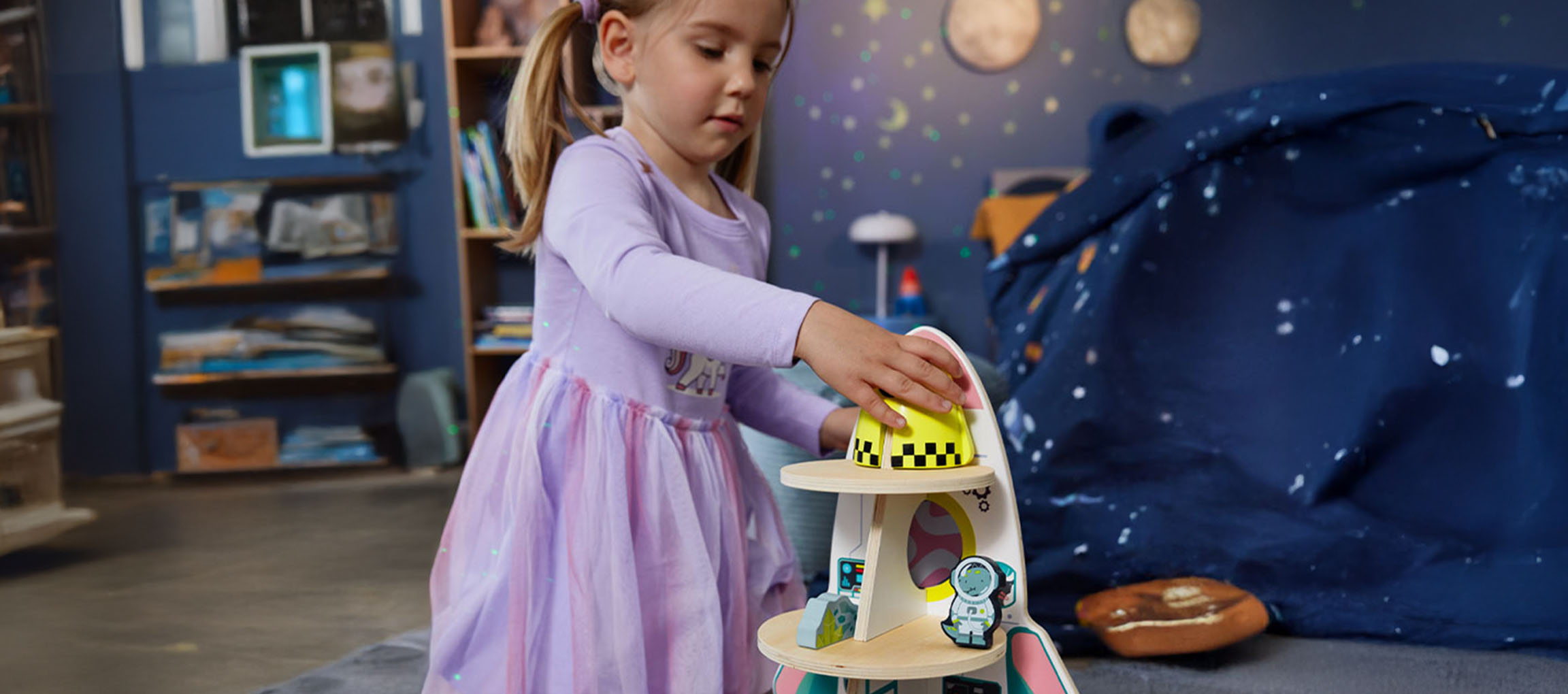 Menina brinca com um brinquedo de nave espacial em um quarto com tema espacial.