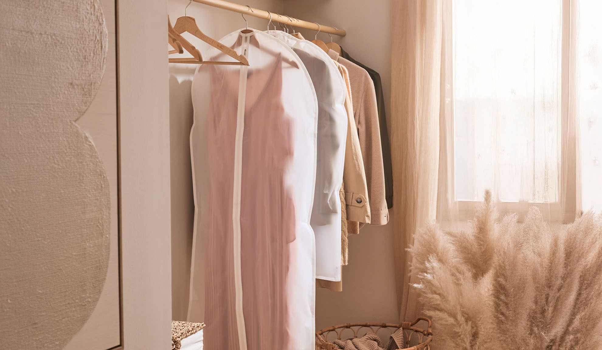 Roupas em sacos de vestuário transparentes penduradas num varão de cabides num quarto claro.