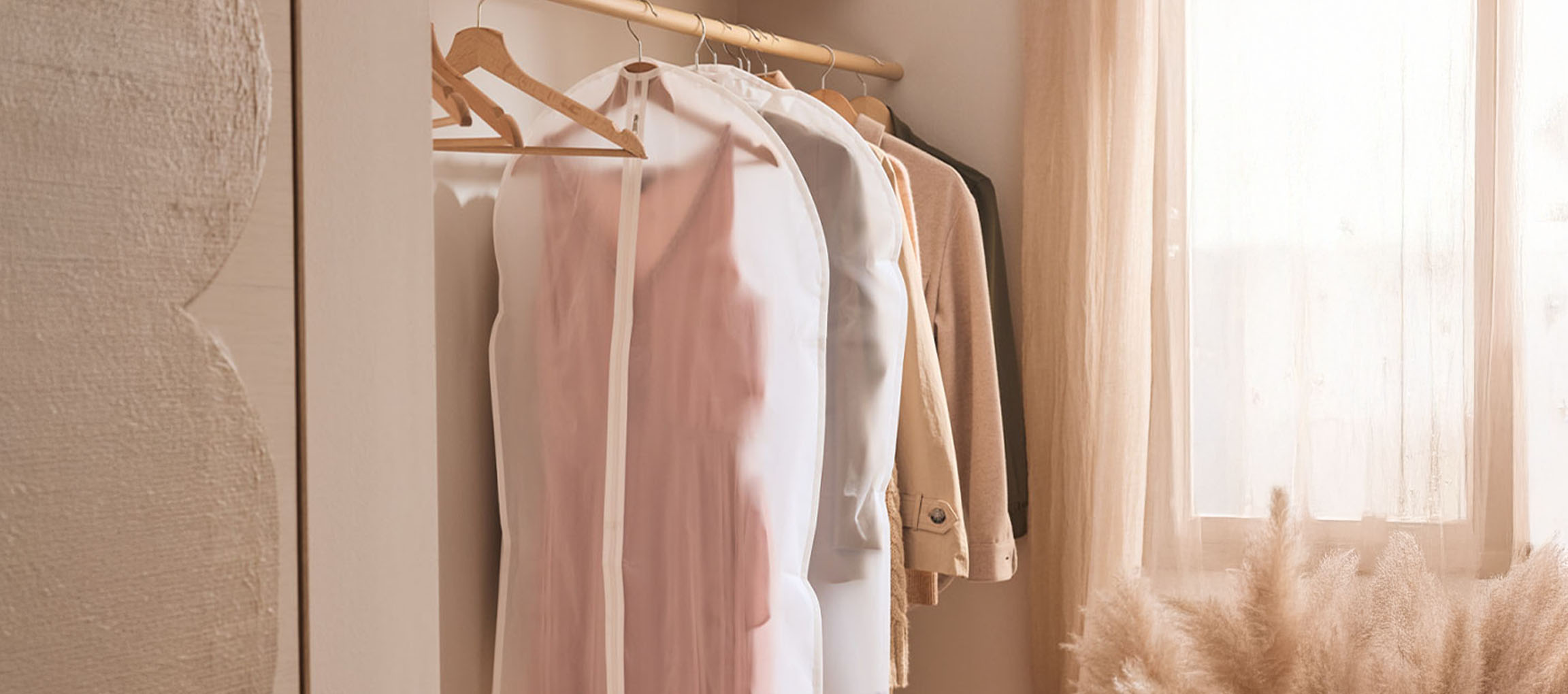 Sacos de roupa e roupas em cabides num armário junto a uma janela.