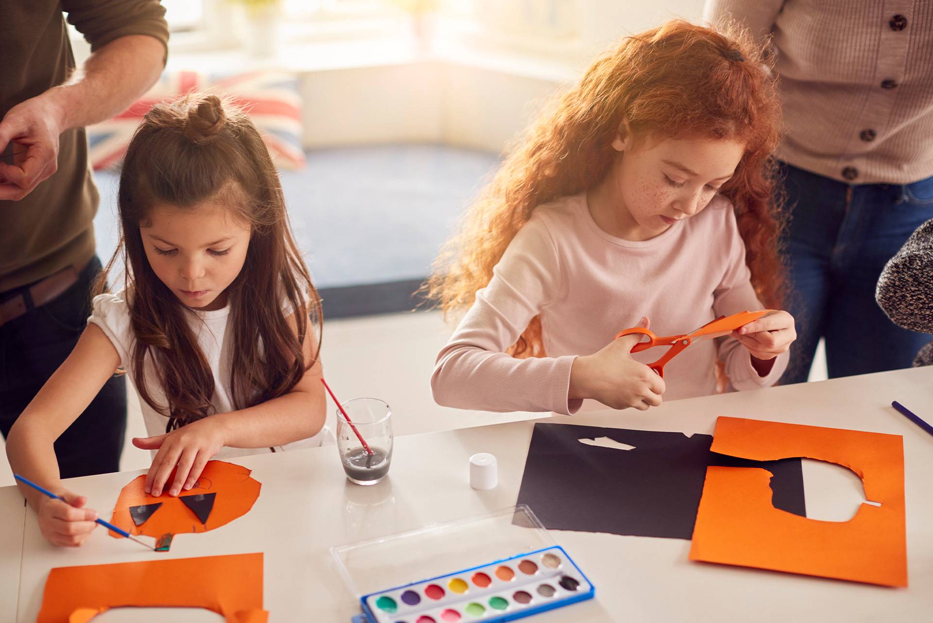 Duas meninas a criar decorações de Halloween com papel e tintas.