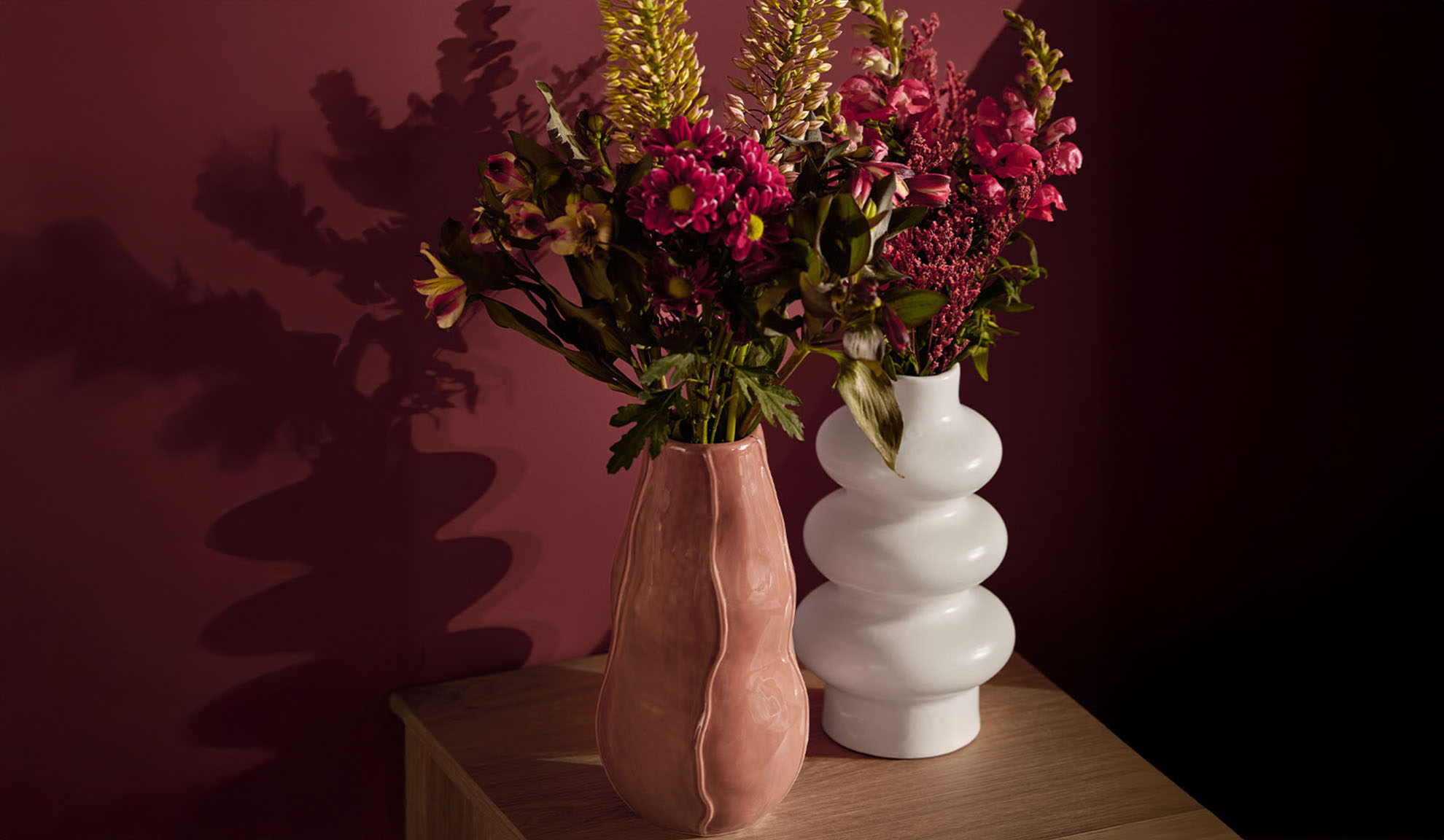 Duas jarras com flores coloridas sobre uma mesa de madeira.