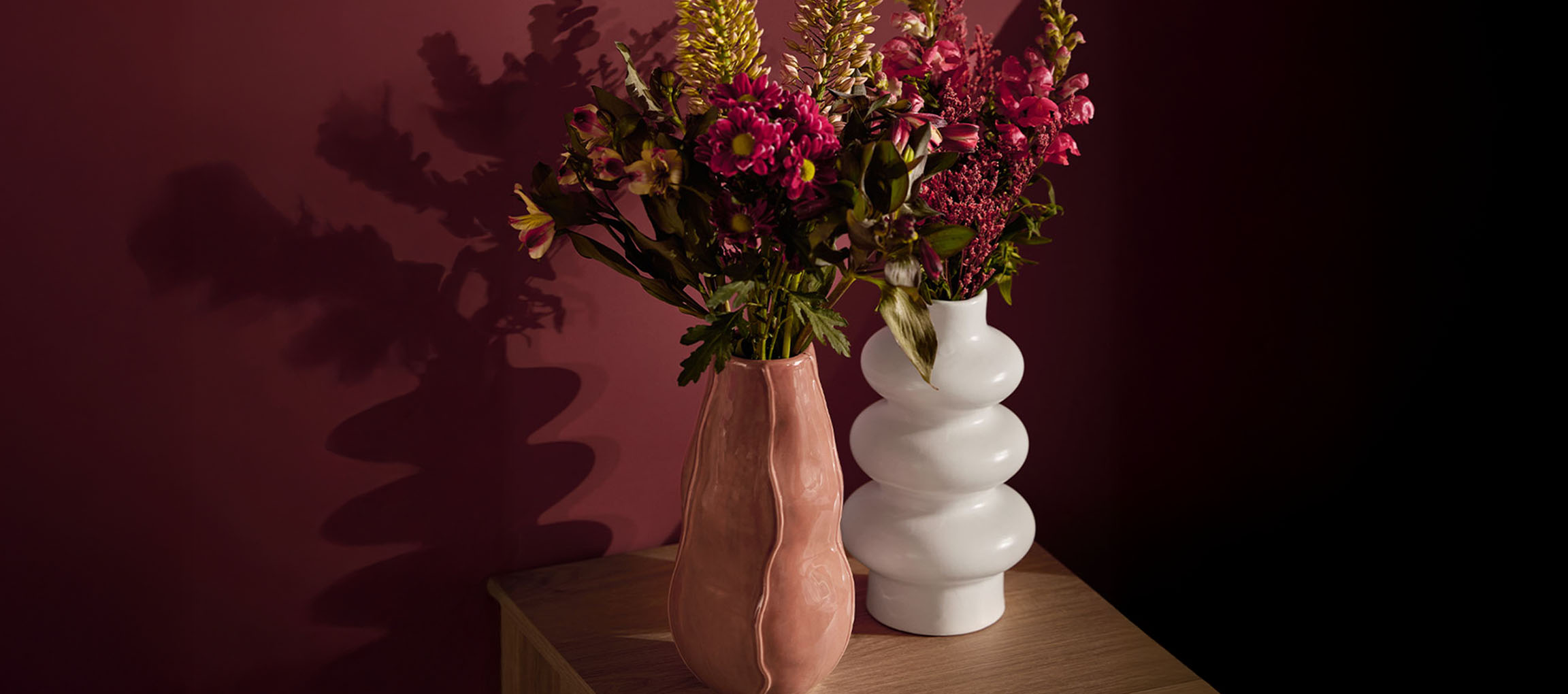 Duas jarras com flores, uma rosa e uma branca, sobre uma superfície de madeira.
