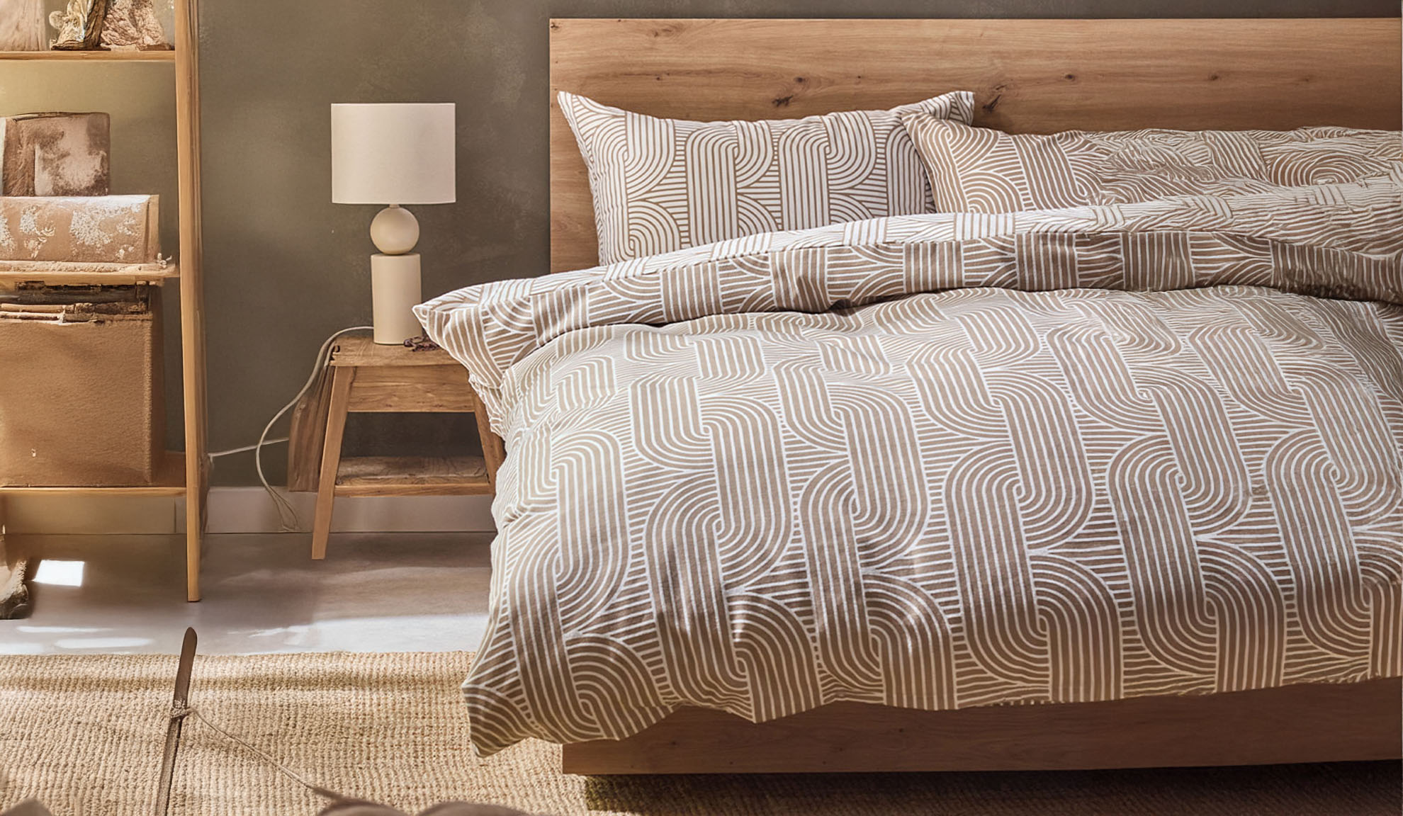 Quarto com cama de madeira, roupa de cama com padrão geométrico e mesa de cabeceira com candeeiro.
