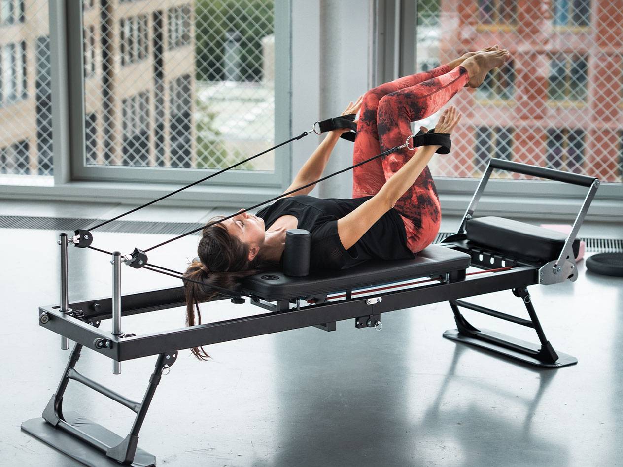 Mulher a fazer Pilates num reformer com calças de ioga vermelhas.
