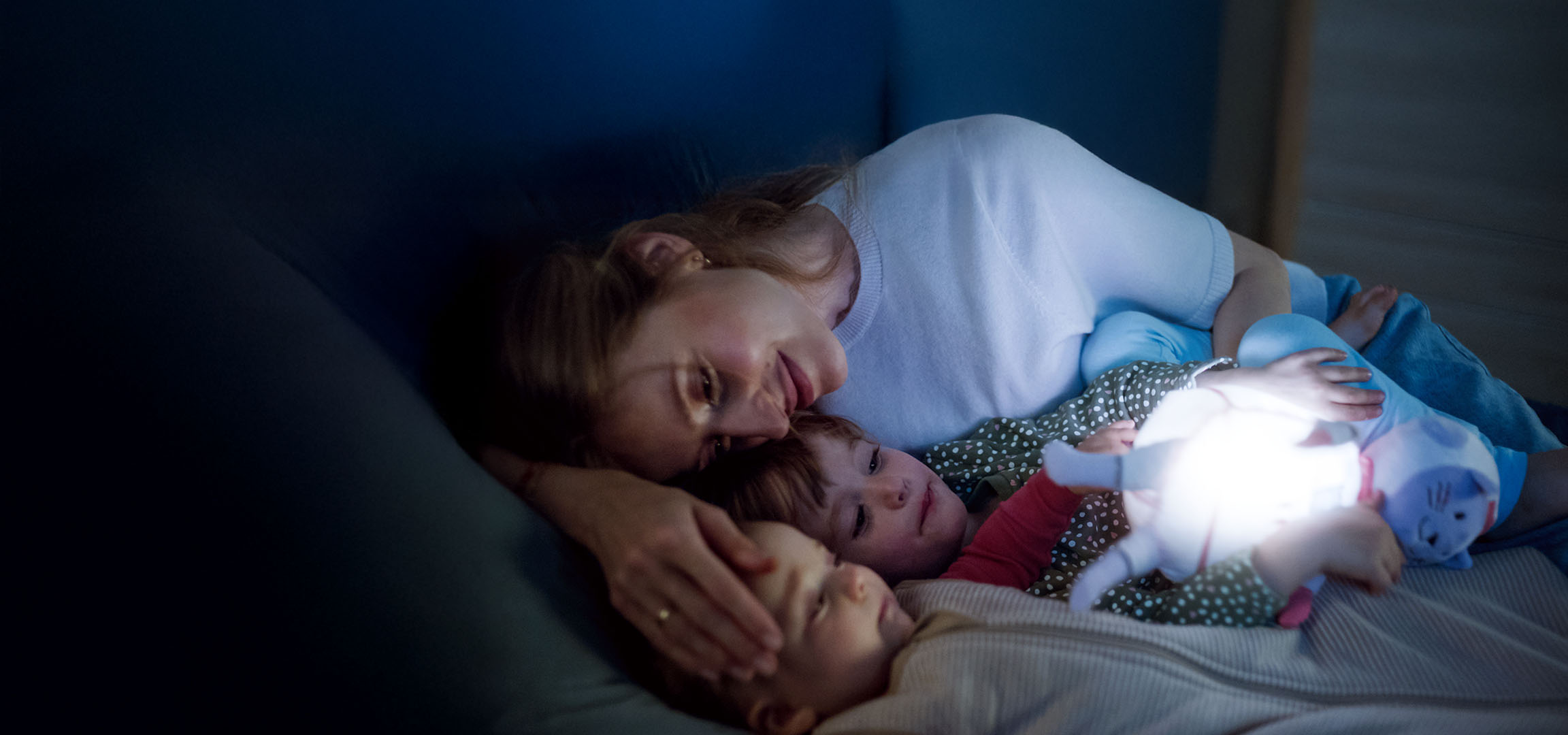 Mãe e dois filhos na cama com um brinquedo luminoso