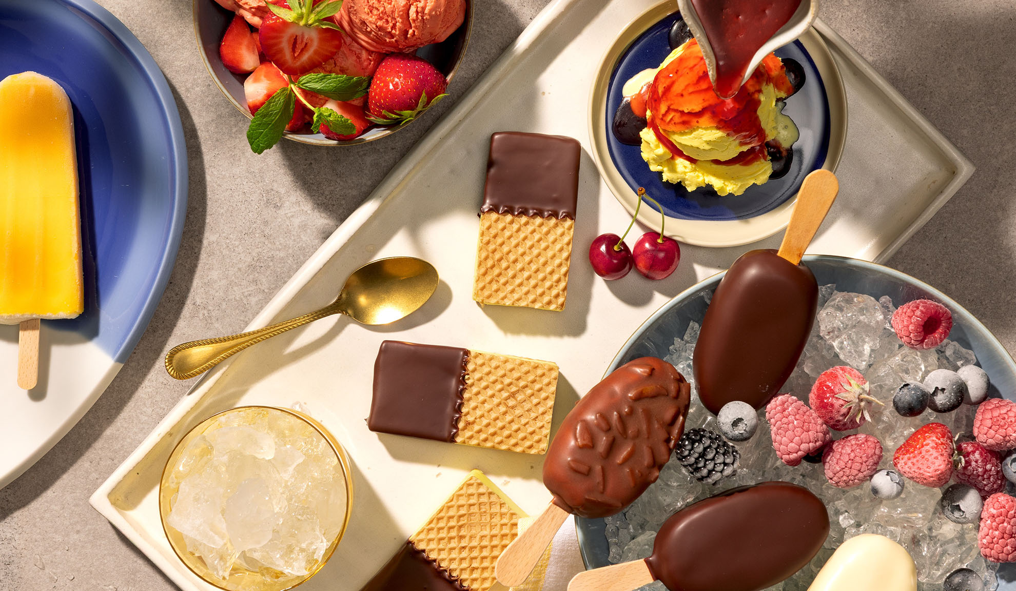 Variedade de gelados, picolés, waffles e bagas numa bandeja.