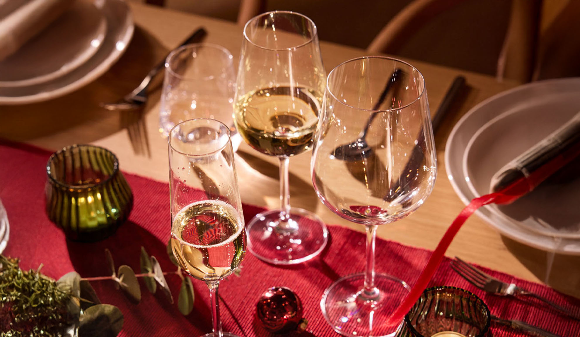 Mesa festiva posta com copos de vinho, taça de champanhe e decorações de Natal.